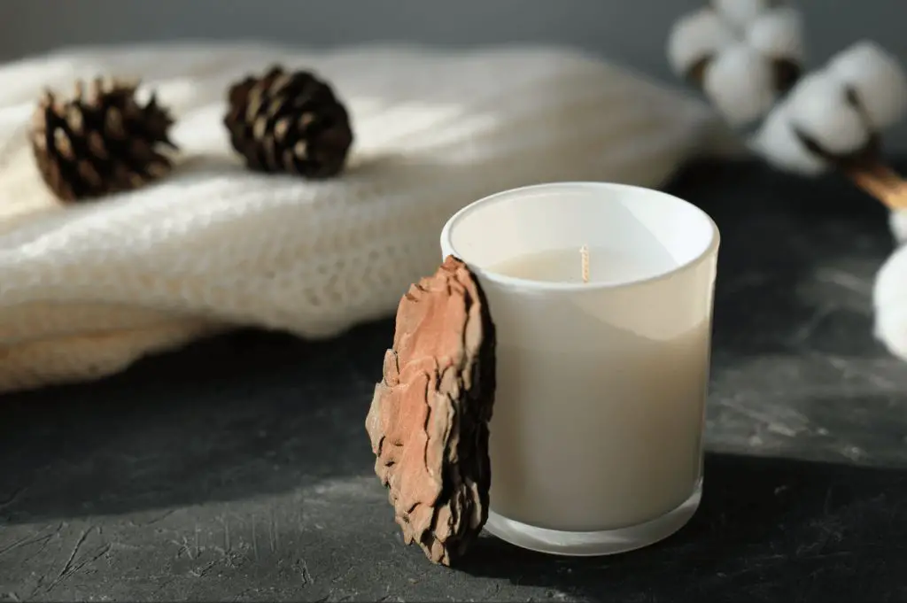 white soy candle burning on wooden table with essential oil bottles