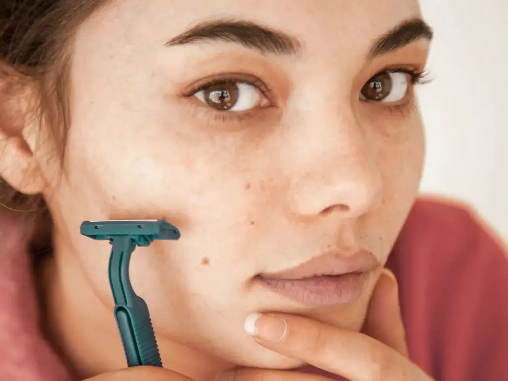 woman shaving facial hair with a razor