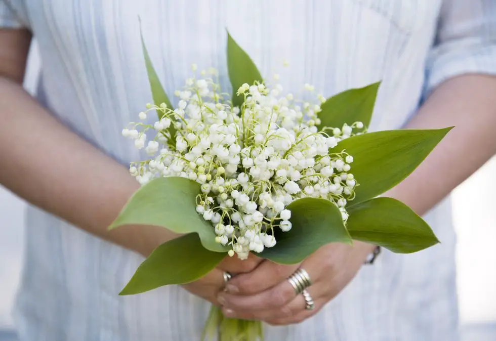 a bride holding a bouquet with lilies of the valley, representing happiness.