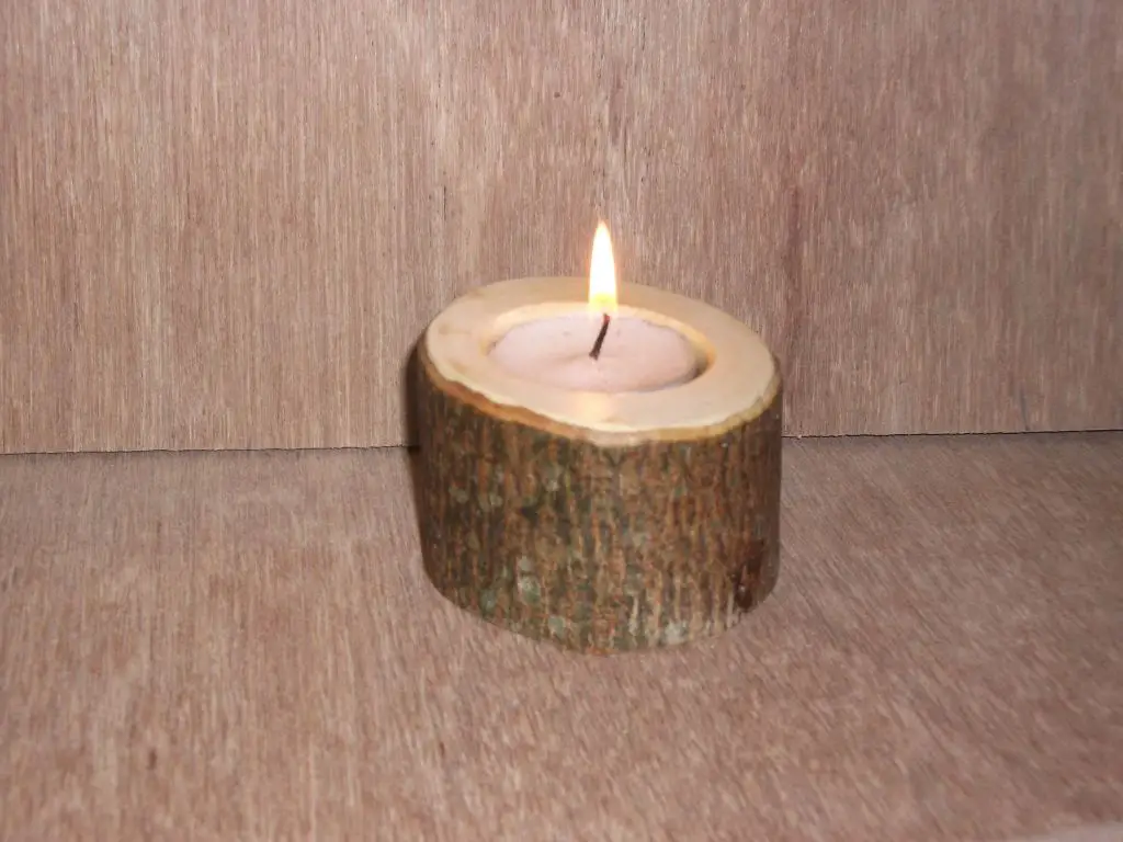 a burning candle held in an ornate metal candle holder on a wooden table.