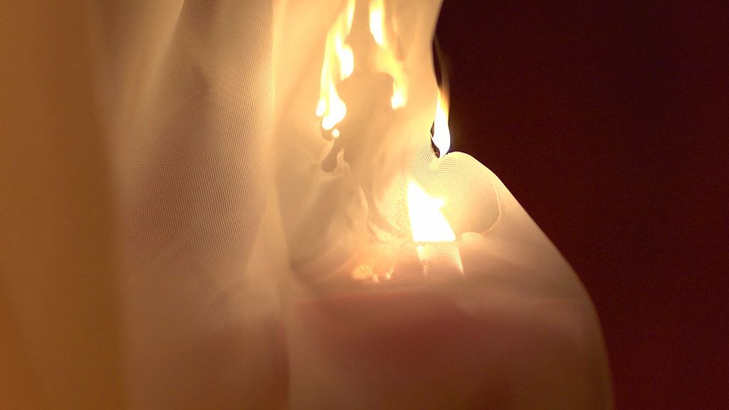 a burning candle placed dangerously close to some curtains in a bedroom.