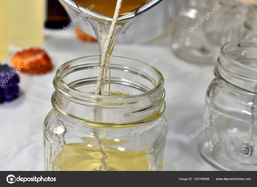 a candle maker pouring wax into a glass jar mold to make a scented candle.