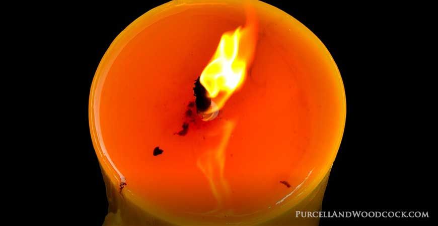 a close up image of a burning candle with melted wax pooling around the wick.