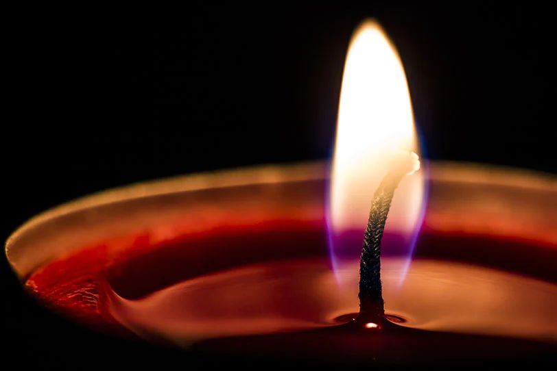 a close up image shows a burning candle with a wick that is too short, creating a small weak flame and tunneling down the center of the wax.