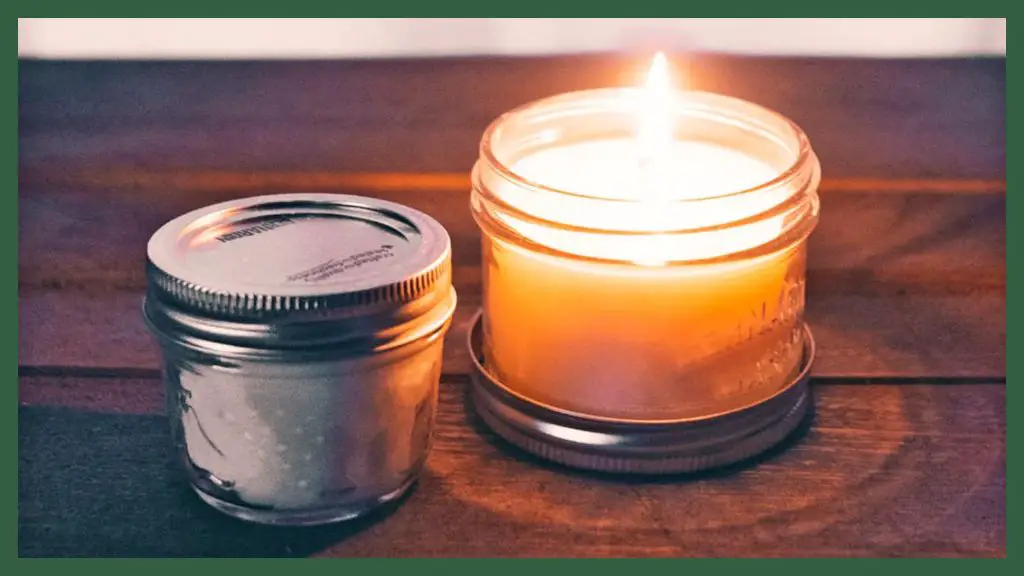 a homemade candle with a wax-coated wick burning inside a glass jar.