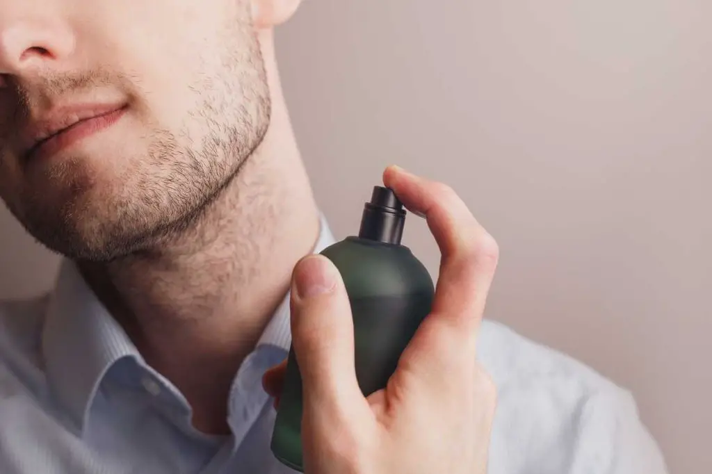 a man spraying on cologne at his neck pulse points.