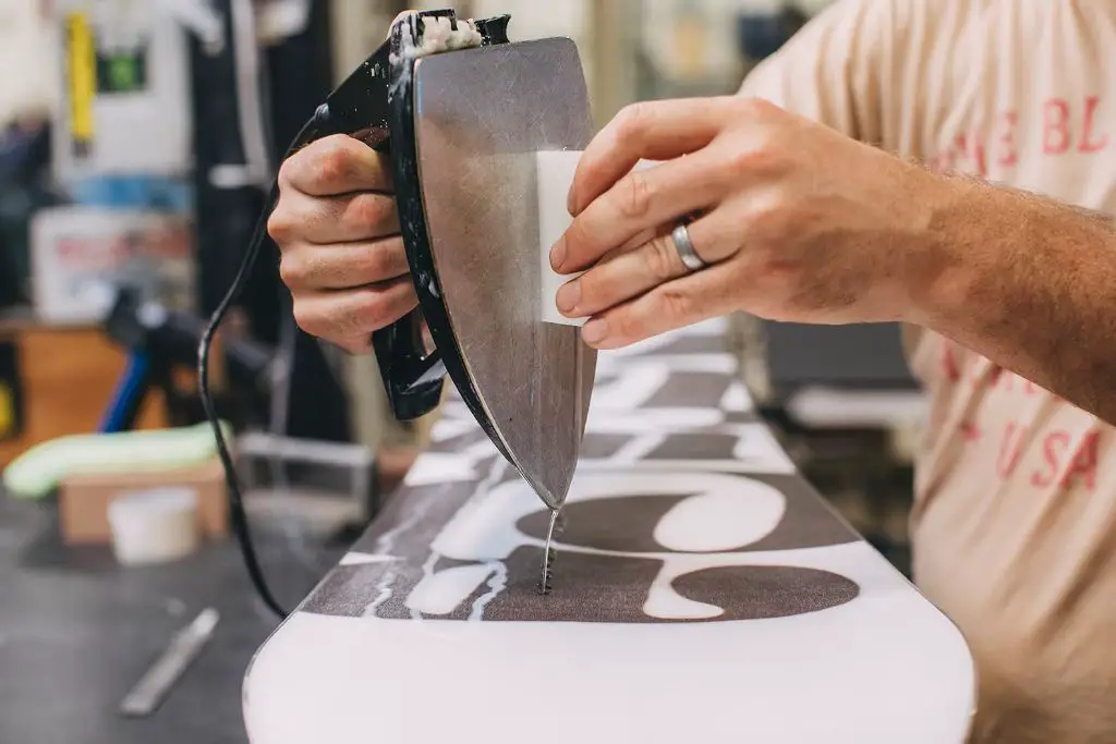 a person applying a layer of white paraffin wax to the bottom of a snowboard before going snowboarding.