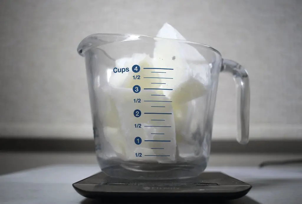 a person carefully measuring melted wax by volume using a pyrex measuring cup.