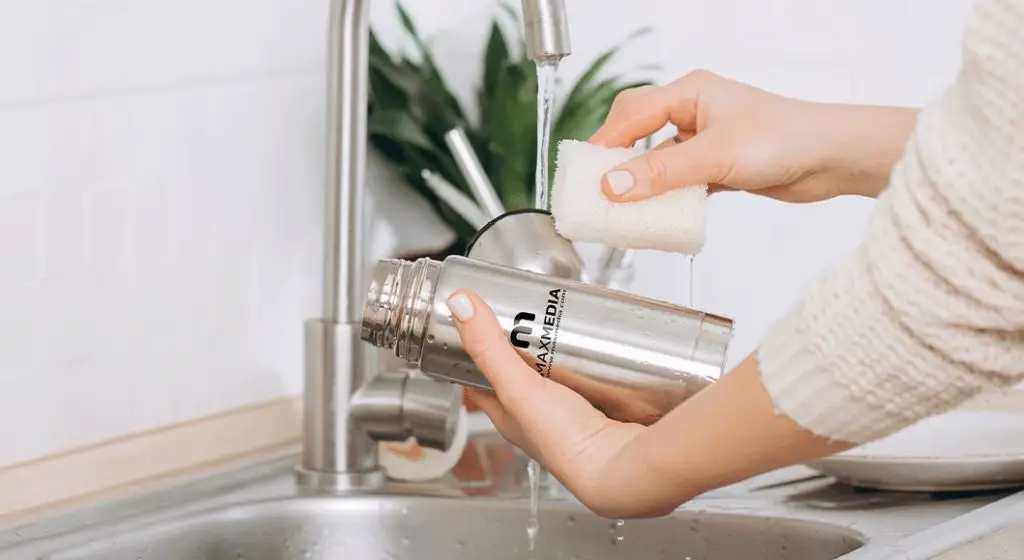 a person handwashing a tervis tumbler in a sink