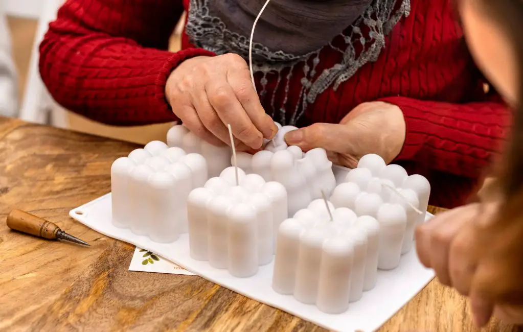 a person pouring melted beeswax into a candle mold with a wick.