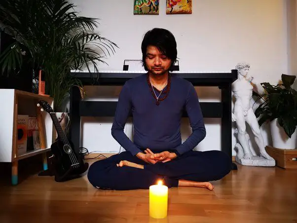 a person sitting in a meditative pose, eyes closed, with a blue candle lit in front of them.