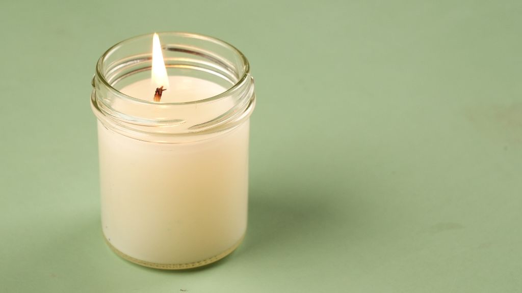 a person using a kitchen spoon to gently scrape and smooth wax on top of a jar candle.