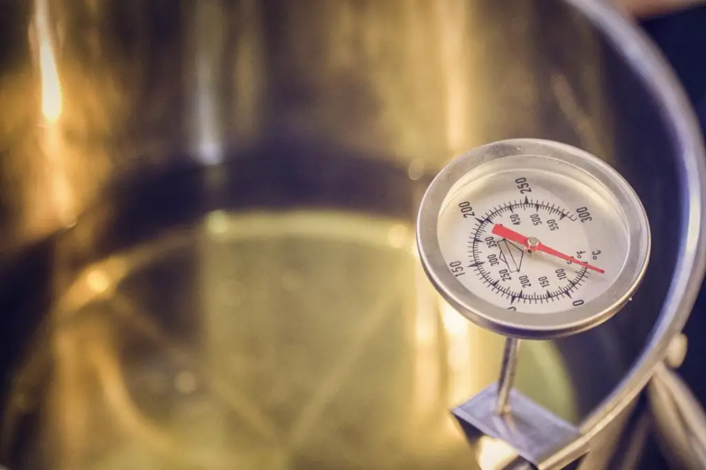 a person using a thermometer to test the smoke point of oil heating in a pan.