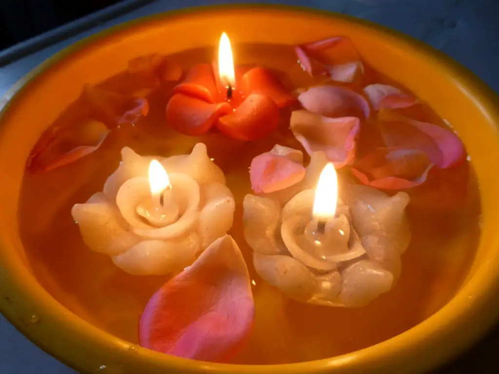 a person wearing gloves while pouring melted candle wax into a container