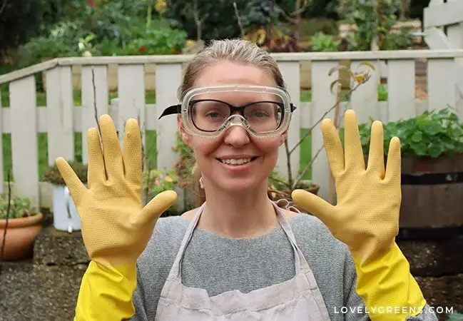 a person wearing goggles, gloves, and an apron while mixing soap ingredients.