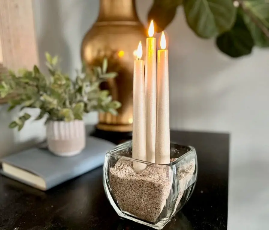 a pillar candle surrounded by sand in a glass bowl to hold it upright