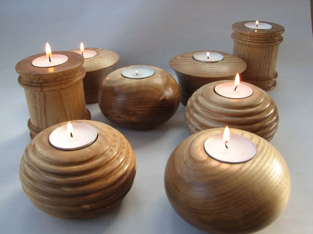 a round wooden tea light holder with a burning candle inside that emits a warm, cozy glow.