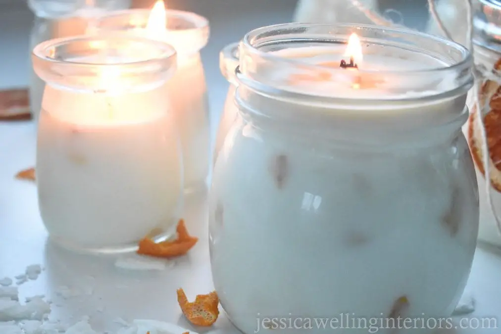 a variety of colorful soy candles with cotton wicks standing in glass jars on a wooden table.