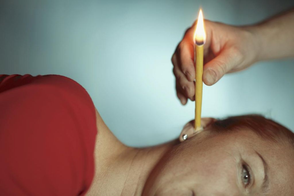 an ear candle next to a human ear, showing the risk of hot wax burns