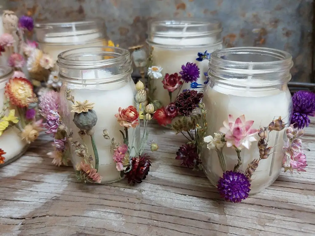 mason jar candle with dried flowers and herbs inside the wax.