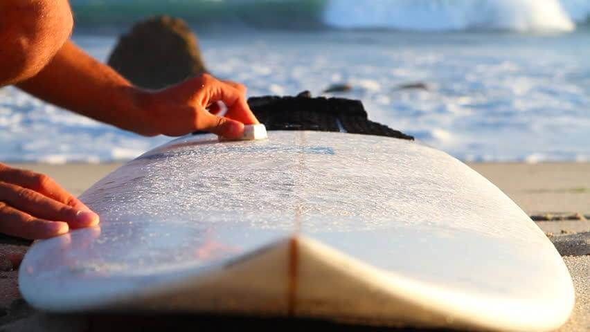 person dipping their fingers into a tub of surf wax to apply to their surfboard