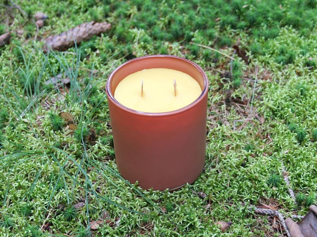 person lighting a beeswax candle with a wood wick