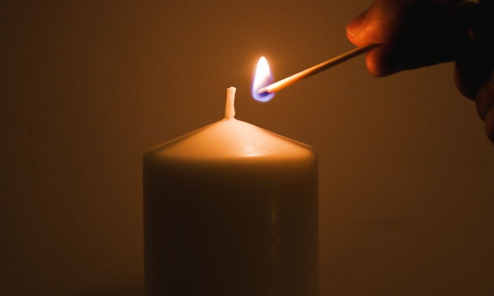 person lighting a candle wick with a match.
