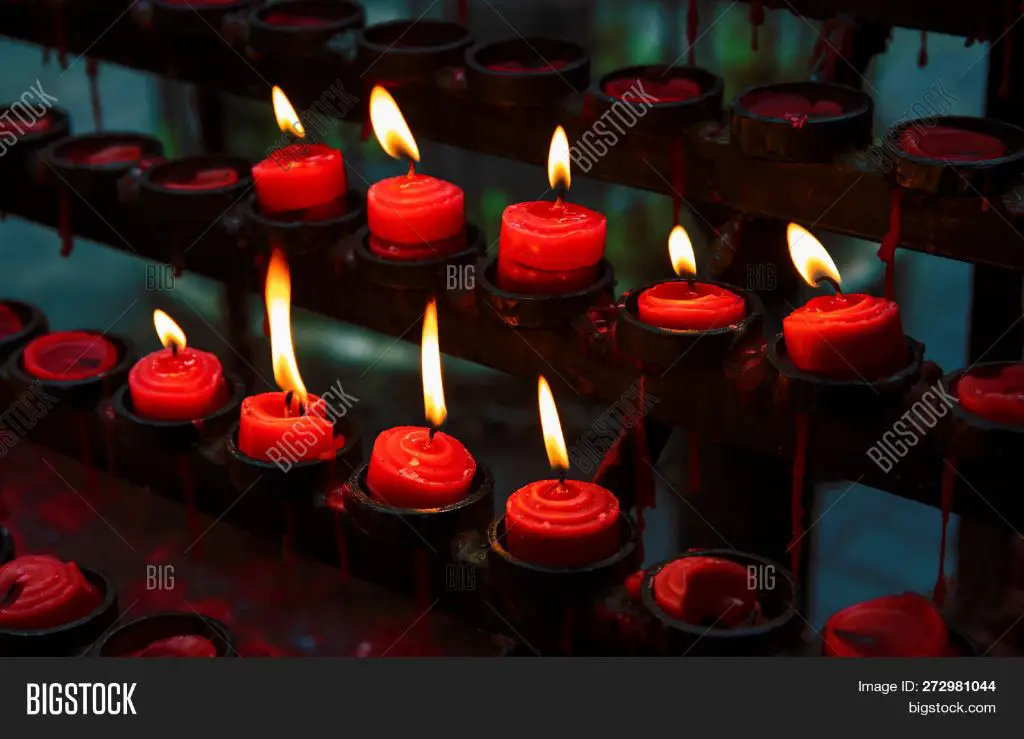 person lighting a red candle on an altar.