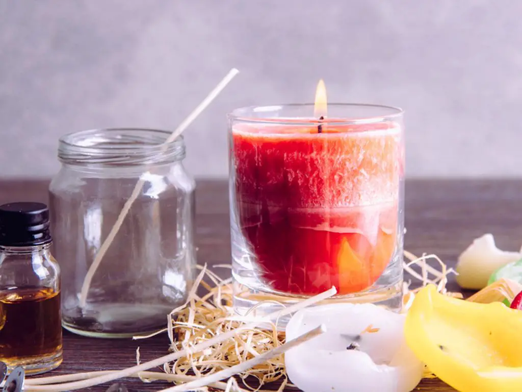 person pouring melted wax into a glass jar.