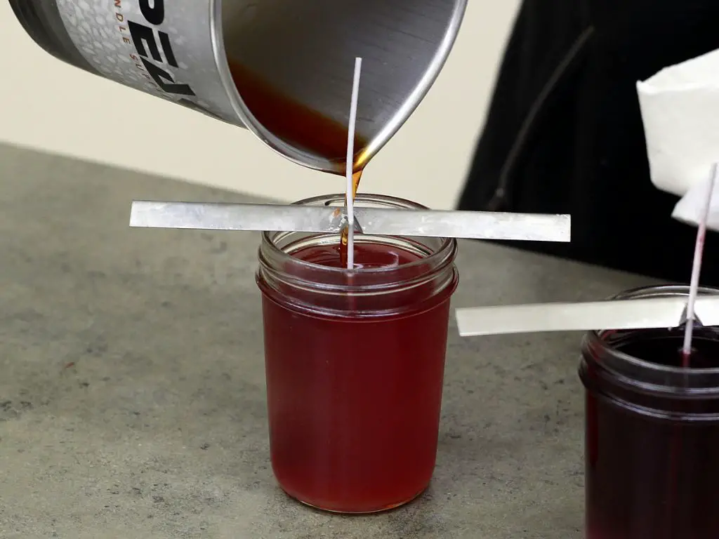 person pouring soy candle wax into a glass container