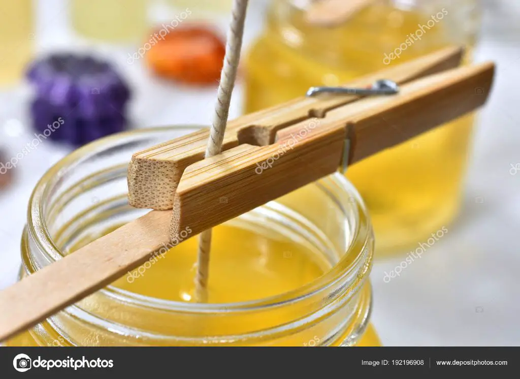 person pouring yellow soy wax into a glass jar candle mold