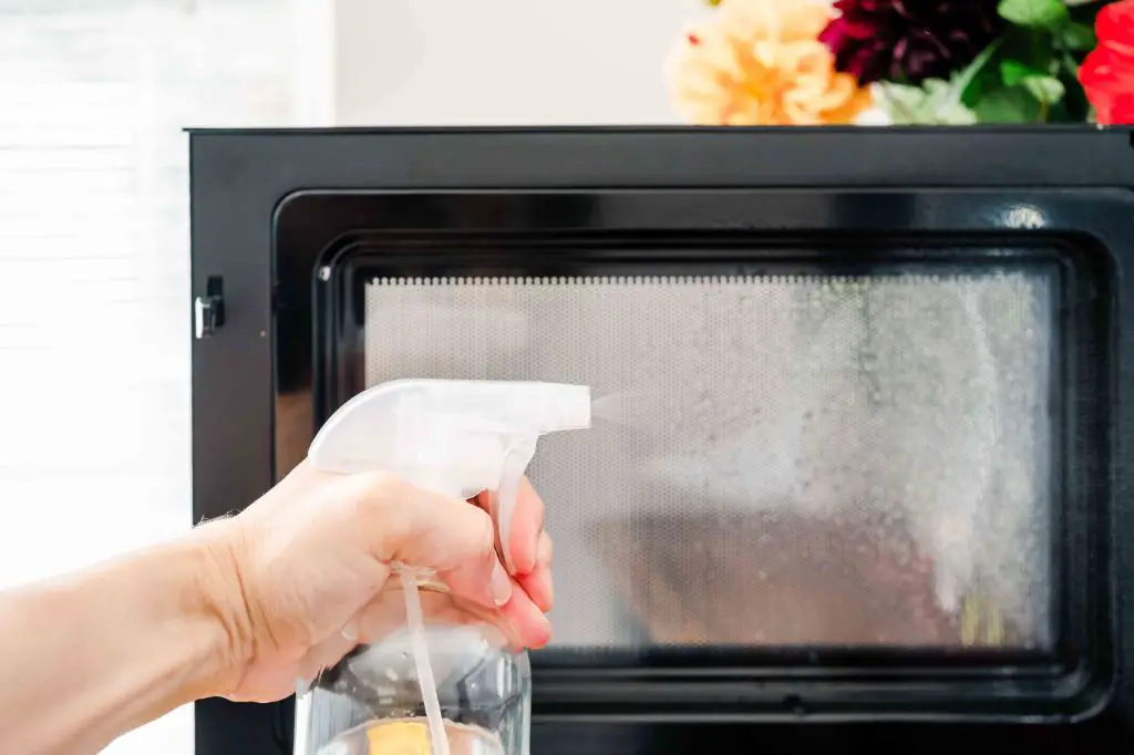 person wearing oven mitts and carefully removing a glass container of melted wax from the microwave