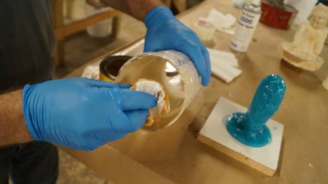 person wearing protective gloves carefully pouring hot wax into a silicone mold