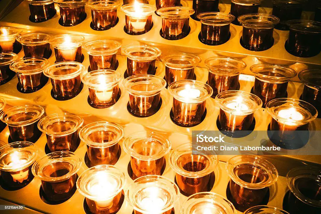 rows of votive candle holders with candles lit inside a church.