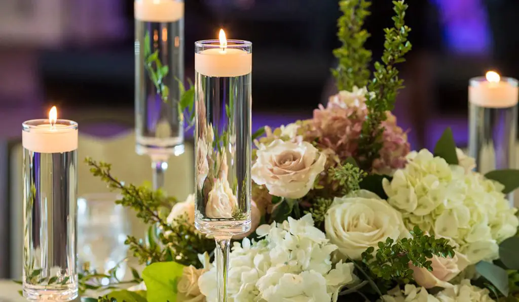 small roses floating around an ornate glass candle holder with a lit floating candle.