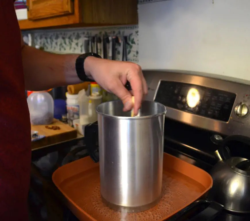 someone melting candle wax in a stainless steel pot on a stove.