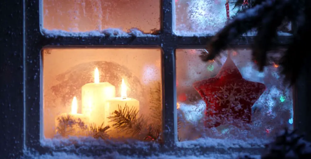 a candle shining in a frosty window represents christmas welcome and hope.