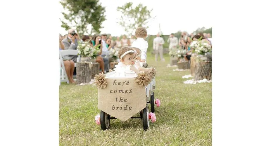 Two flower girls being pulled by a ring bearer on a wagon with the sign, ‘Here comes the bride’ – this is cuteness overload!